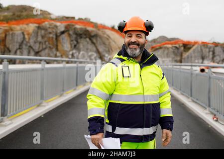 Porträt eines männlichen Ingenieurs in reflektierender Kleidung, die auf einer Brücke steht Stockfoto