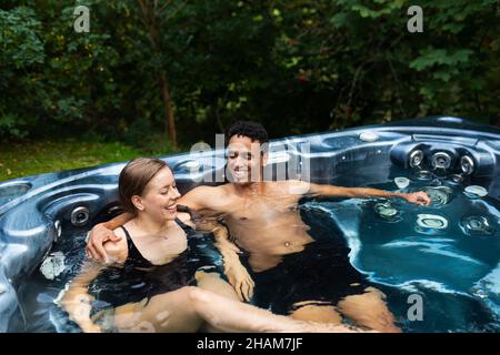 Lächelndes junges Paar, das im Whirlpool sitzt Stockfoto