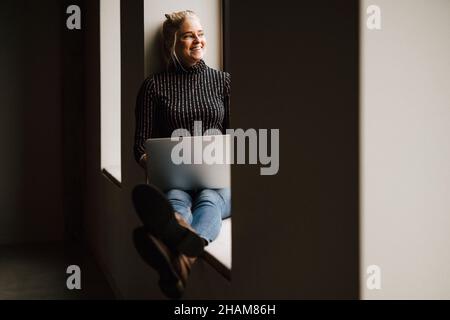Lächelnde Frau, die auf dem Fensterbrett sitzt Stockfoto
