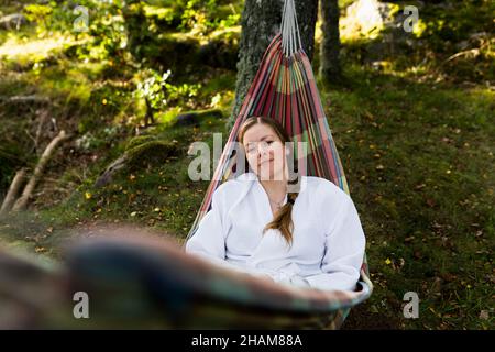 Junge Frau im Bademantel, die sich in der Hängematte entspannt Stockfoto