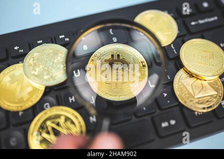 Nahaufnahme der Bitcoin-Münzen durch die Lupe auf der Tastatur neben der beliebten Kryptowährung Ethereum, Binance, Cardano, Zcash. Konzept der Krypto-Marktanalyse. Stockfoto