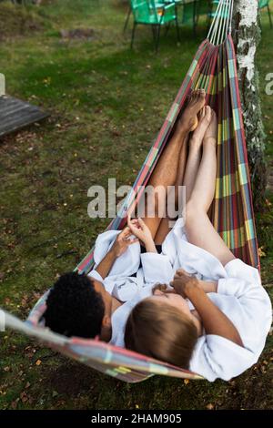 Junges Paar in Bademänteln, das sich in der Hängematte entspannt Stockfoto