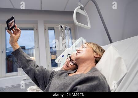 Erwachsene Tochter nimmt Selfie mit Mutter auf Krankenhausbett Stockfoto