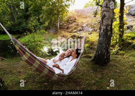 Junges Paar in Bademänteln, das sich in der Hängematte entspannt Stockfoto