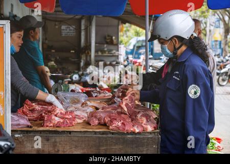 In der Freilufttheke einer Metzgerin auf dem Straßenmarkt. Die Käuferin wählt das Fleisch. Da Lat, Vietnam: 2021-05-08 Stockfoto