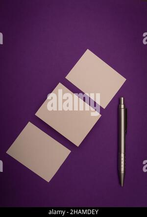 Drei leere Visitenkarten und ein Stift auf violettem Hintergrund, imitierte Branding. Stockfoto