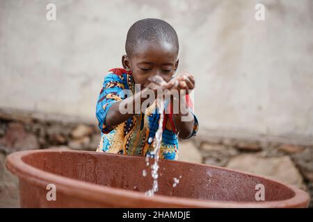 Nahaufnahme junger durstiger afrikanischer Junge in afrikanischen Vororten genießt frisches, sauberes Wasser aus dem Eimer Stockfoto