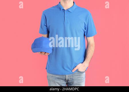 Mann in blankem blauem Polo hält Mütze auf rosa Hintergrund Stockfoto