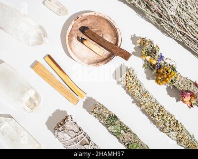 Gegenstände für die spirituelle Reinigung - Salbei- und aromatische Kräuterbündel, palo santo-Räucherstäbchen und Quarzkristalle auf weißem Grund. Draufsicht. Flach liegend Stockfoto