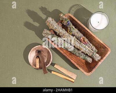 Sammelartikel für die spirituelle Reinigung - aromatische Kräuterbündel, palo santo Räucherstäbchen und Kerze auf grünem Hintergrund. Draufsicht. Flach liegend Stockfoto