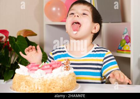 Das Kind feiert Geburtstag, lacht und leckt, isst einen Geburtstagskuchen. Stockfoto