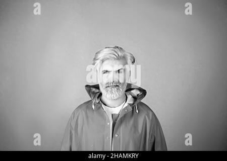 Porträt eines reifen Mannes mit gelben Haaren in einem gelben Regenmantel isoliert auf gelbem Hintergrund. Stockfoto