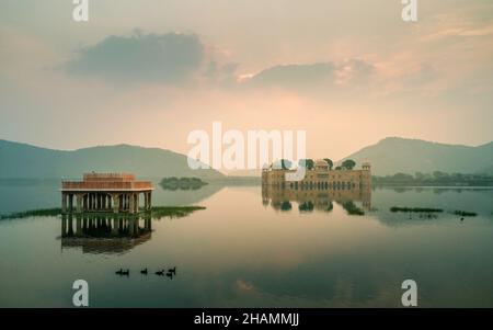 Blick über ruhigen See mit verlassenen Königspalast von See und Aravalli Hügel umgeben als Morgengrauen bricht in Jaipur, Rajasthan, Indien. Stockfoto