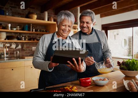 Multikulturelles, älteres Paar lächelt und kocht Frühstück in einer modernen Küche. Glückliches Paar zog sich zu Hause zurück. Stockfoto