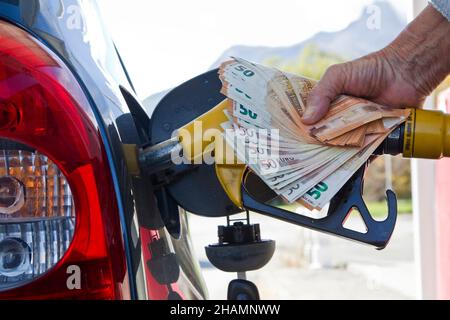 Illustration zum Anstieg der Pumpenpreise. Jemand, der an einer Tankstelle einen Tank mit Benzin befüllt. Sie hält eine Benzinpumpe und eine Bank mit einem Geldpaket von 50 Euro Stockfoto