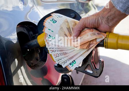 Illustration zum Anstieg der Pumpenpreise. Jemand, der an einer Tankstelle einen Tank mit Benzin befüllt. Sie hält eine Benzinpumpe und eine Bank mit einem Geldpaket von 50 Euro Stockfoto