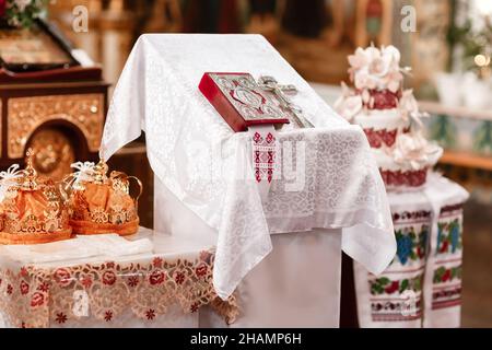 Zwei Kronen die Hochzeiten, die für die Zeremonie in der orthodoxen Kirche bestimmt sind. Orthodoxe Hochzeitszubehör Heilige Bibel und silbernes Kreuz. Stockfoto