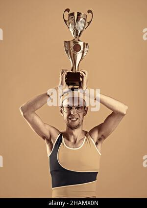 Glücklicher Sieger drückt sich den Siegerpokal auf gelbem Hintergrund zu. Stockfoto