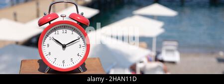 Roter Wecker um 10 Uhr morgens vor dem Hintergrund des Strandresorts Stockfoto