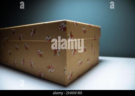 Ein Weihnachtsgeschenk auf einem weißen Tisch mit blauem Hintergrund. Neujahr Geschenke. Geschenk in Karton mit roten Elementen. Frohes neues Jahr Stockfoto
