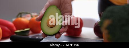 In der Frau liegen handgeschnittenes reifes Avocado-Messer und Gemüse auf dem Tisch. Stockfoto