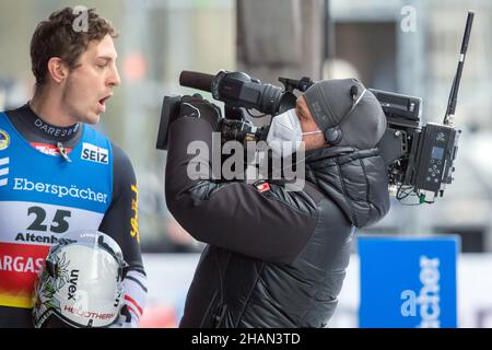 Altenberg, Deutschland. 12th Dez 2021. Rennrodel: WM, Einzelperson, Männer, zweiter Lauf. Ein Kameramann steht vor Reinhard Egger aus Österreich im Zielbereich. Quelle: Sebastian Kahnert/dpa-Zentralbild/ZB/dpa/Alamy Live News Stockfoto