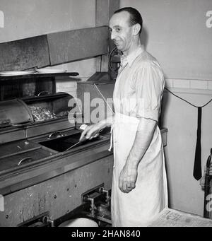 1951, historisch, ein männlicher Kaffeehaus-Besitzer in seiner Küche, mit einer Taille oder einer halben Schürze, der an der Fritteuse beim Kochen von Speisen stand, London, England, Großbritannien. Stockfoto
