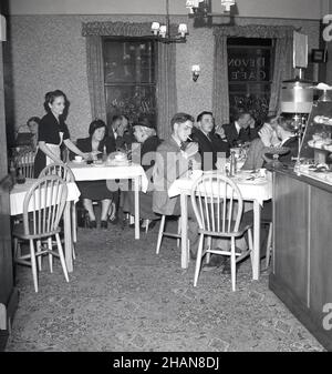 1950s, historisch, Kunden im oberen Essbereich eines Cafés der Ära, sitzen an mit Stoff bedeckten Tischen, Bedienung und mit einem Zähler mit Kuchen im Angebot, UK.das Fruchtgetränk, Qoush ist neben dem Schalter erhältlich. Quosh war ein aromatisierter Squash oder schwacher Cordial, dem Wasser hinzugefügt wurde und wurde erstmals im Vereinigten Königreich im Jahr 1950s in den Geschmacksrichtungen Orange, Gerstenwasser und Zitrone hergestellt. Stockfoto