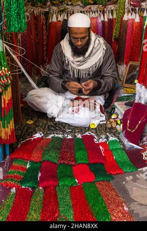 Ein muslimischer Nepalesischer hält die Schnur an den Zehen, während er im Potey Bazaar in Kathmandu, Nepal, eine Perlenkette macht. Stockfoto