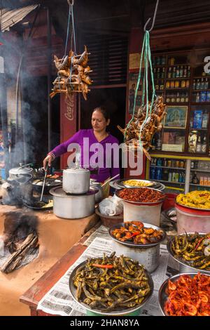 Eine Frau kocht auf einem Chulo oder einem traditionellen Holzofen im Freien aus Schlamm in einem Restaurant am Straßenrand in Malekhu, Nepal. Stockfoto