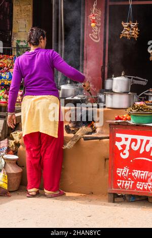 Eine Frau kocht auf einem Chulo oder einem traditionellen Holzofen im Freien aus Schlamm in einem Restaurant am Straßenrand in Malekhu, Nepal. Stockfoto