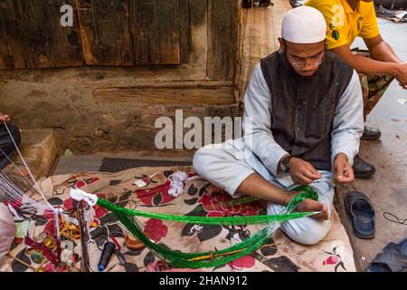 Ein muslimischer Nepalesischer hält die Schnur an den Zehen, während er im Potey Bazaar in Kathmandu, Nepal, eine Perlenkette macht. Stockfoto