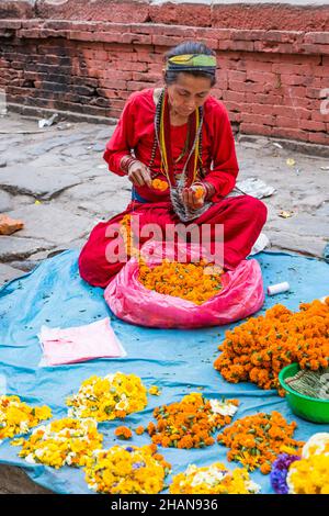 Eine nepalesische Frau schnüren Blumen, um Girlanden für religiöse Opfer in Hindu-Tempeln in Kathmandu, Nepal, zu machen. Stockfoto