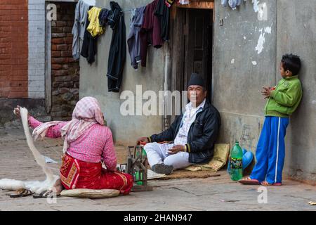 Eine nepalesische Familie, die vor ihrem Haus im mittelalterlichen Dorf Khokana in Newari sitzt. Kathmandu Valley in Nepal. Die Frau dreht den Faden wi Stockfoto