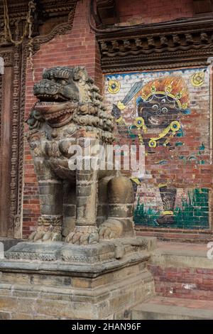 Ein steinerner Hüterlöwe vor dem alten königlichen Palast auf dem Durbar Square, Patan, Nepal. Dahinter ist ein Gemälde des Schwarzen Bhairabs. Stockfoto