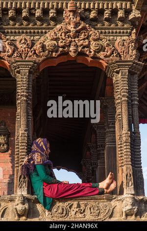 Eine nepalesische Frau in traditioneller Kleidung sitzt vor dem Harishankar-Tempel, einem Hindu-Tempel auf dem Durbar Square, Patan, Nepal. Stockfoto