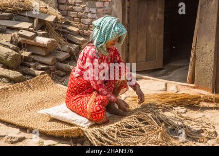 Eine nepalesische Frau webt vor ihrem Haus im mittelalterlichen Dorf Khokana in Newari im Kathmandu-Tal in Nepal eine Jutematte. Stockfoto