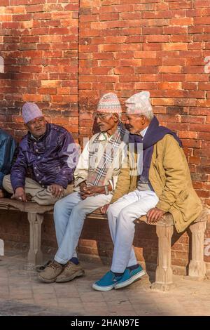 Drei ältere nepalesische Männer mit traditionellen dhaka-Topi-Hüten sitzen auf einer Bank zusammen auf dem historischen Durbar Square in Patan, Nepal. Stockfoto