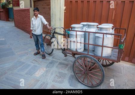 Ein junger Mann aus Nepal, der große Metallmilchbecher in einem Dreiradwagen in Kathmandu, Nepal, trägt. Stockfoto