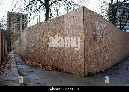 Eine Stadtgasse mit einer Backsteinmauer und einer Spanplatte von einer Baustelle, die eine unheimliche Szene schafft, die konzeptuell genutzt werden könnte. Stockfoto