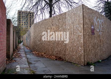 Eine Stadtgasse mit einer Backsteinmauer und einer Spanplatte von einer Baustelle, die eine unheimliche Szene schafft, die konzeptuell genutzt werden könnte. Stockfoto