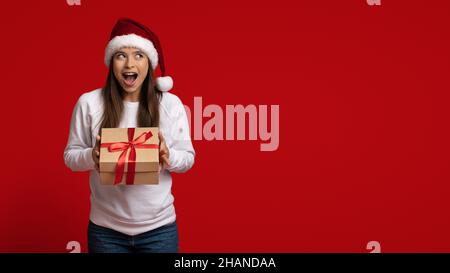 Urlaubsbonus. Emotionale Junge Frau In Der Geschenkschachtel „Santa Hat Holding“ Stockfoto