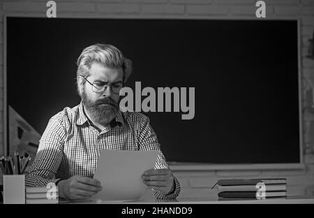 Schöner männlicher Lehrer Überprüfung Hausaufgaben im Klassenzimmer. Stockfoto