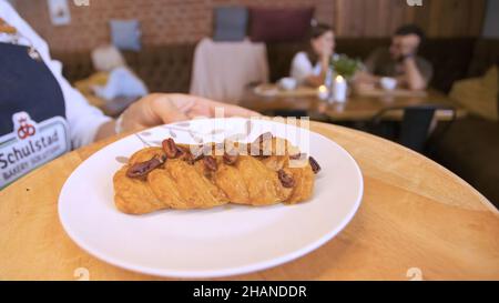 Nahaufnahme der Kellnerin mit Tray. Die Kellnerin trägt ein Tablett mit Croissants im Café. Kellnerin trägt süßes Gebäck auf Tablett mit CO Stockfoto