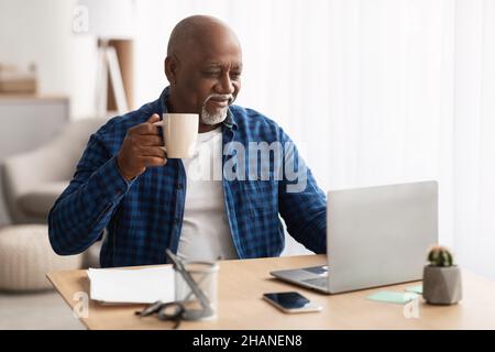 Afroamerikanischer Senior Businessman Trinkt Kaffee Mit Laptop Am Arbeitsplatz Stockfoto