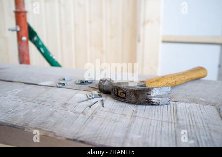 Hammer und Nägel liegen auf dem Gerüst, vor dem Hintergrund einer Wand aus Holzlatten. Arbeitsprozess. Renovierung des Hauses. Stockfoto