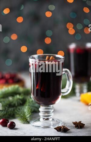 Ein Glas scharf würzigen Glühwein, umgeben von Gewürzen und Zweigen eines Weihnachtsbaums mit Bokeh im Hintergrund. Stockfoto