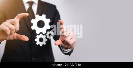 Geschäftsmann im Anzug hält Metallgetriebe und Zahnräder Mechanismus der Interaktion Teamarbeit Konzept, Hand halten Gruppe von virtuellen Zahnräder Rad. Stockfoto