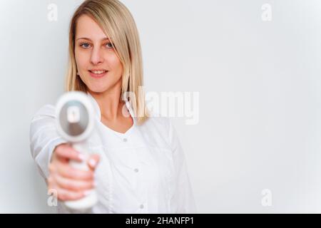 Porträt des Meisters der Laser-Haarentfernung. Frau im weißen Mantel halten Laser-Haarentfernungsvorrichtung in ihren Händen und zeigen als schießen von ihm. Speicherplatz kopieren Stockfoto