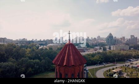 Luftaufnahme eines Kirchturms aus roten Fliesen mit einem goldenen Kreuz. Video. Details eines roten Backsteingebäudes mit einer Stadt und bewölktem Himmel auf der Rückseite Stockfoto